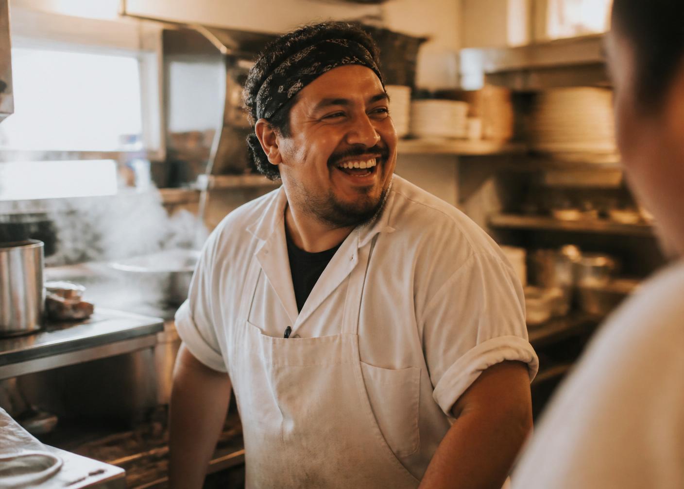 A line cook laughing with a coworker in a bright kitchen